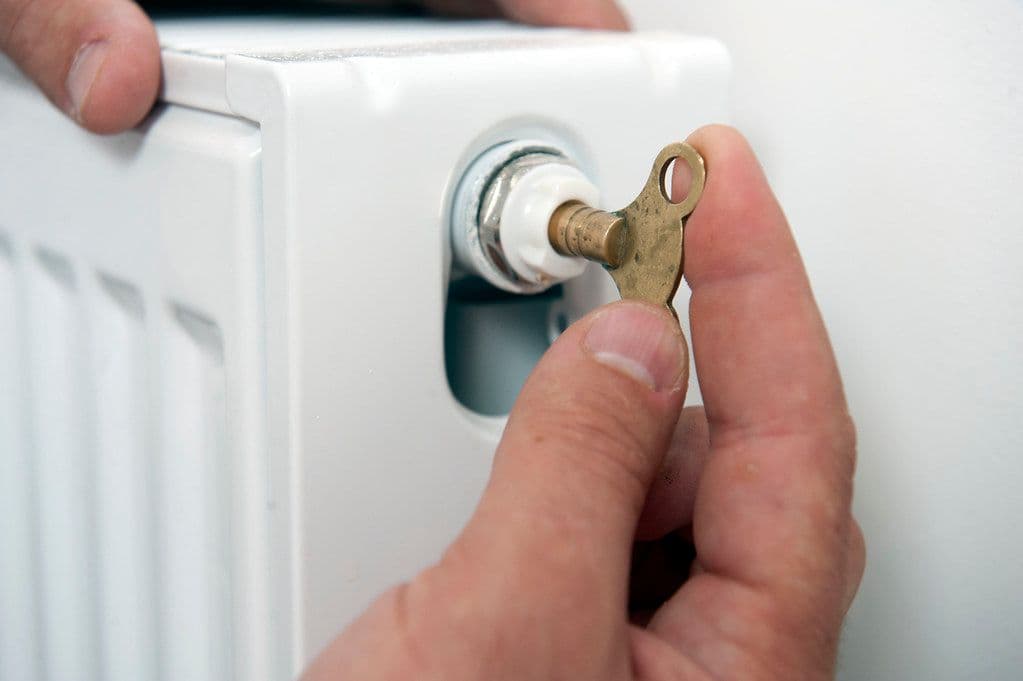 Heating engineer bleeding a radiator during an annual boiler service